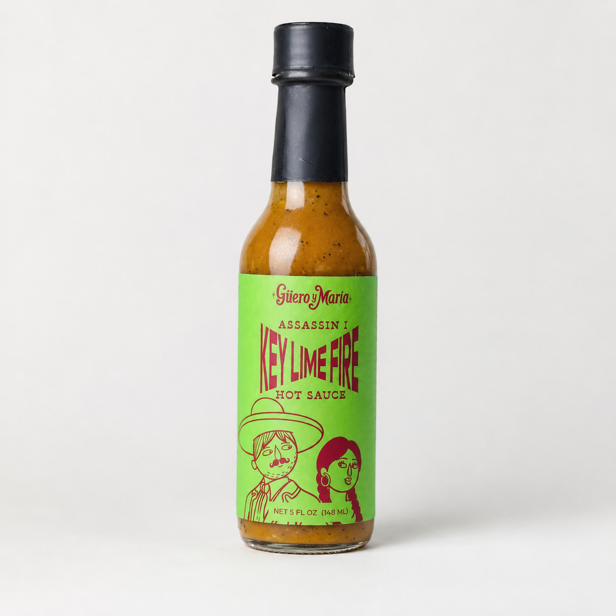 A bottle of Giere Mario 'Assassin' Key Lime Fire' hot sauce, featuring a bright green label with red text and illustrations, topped with a black cap, set against a plain light gray background.